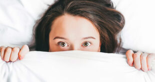 Ragazza a letto sotto le coperte in cui si vedono solo gli occhi